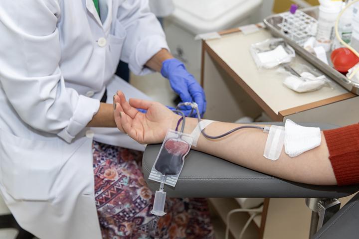 Profissional de saúde acompanha doação de sangue com a bolsa parcialmente cheia conectada ao braço do doador.