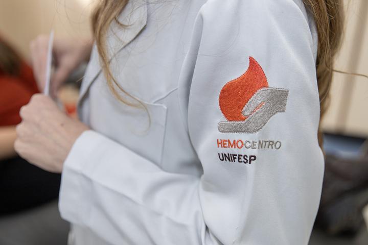 Detalhe do uniforme branco com o logotipo do Hemocentro UNIFESP no braço.