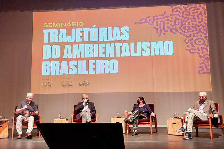 Quatro palestrantes sentados no palco participam de debate no seminário "Trajetórias do Ambientalismo Brasileiro", com telão ao fundo.