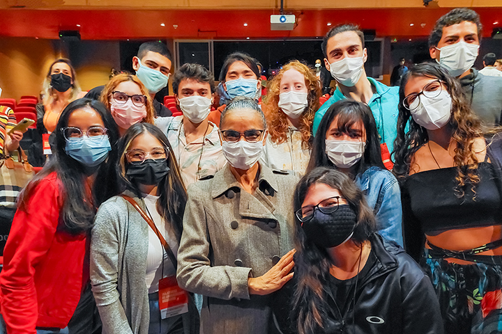 Ministra Marina Silva posa para foto com grupo de jovens usando máscaras em auditório, todos sorrindo.