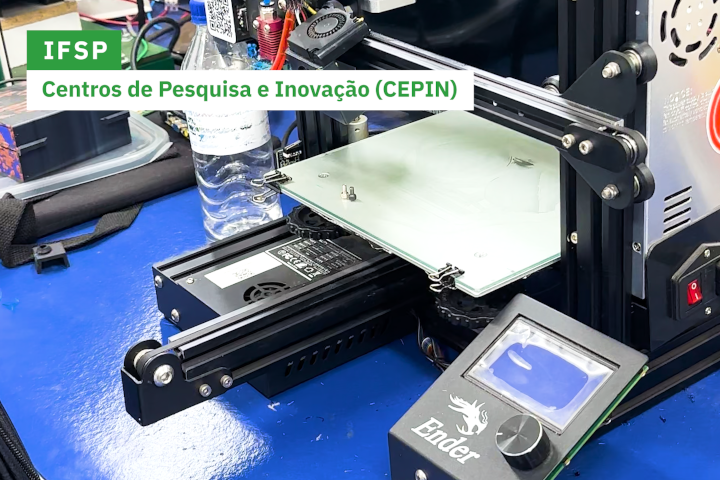 Uma impressora 3D está em funcionamento sobre uma bancada azul, com peças eletrônicas e uma garrafa d’água ao fundo. A imagem destaca o ambiente tecnológico de pesquisa.