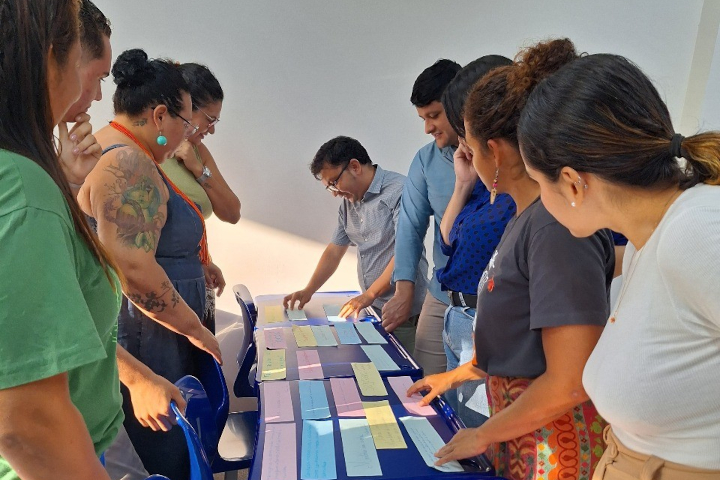 Um grupo de pessoas se debruça sobre uma mesa, olhando e organizando papéis coloridos.