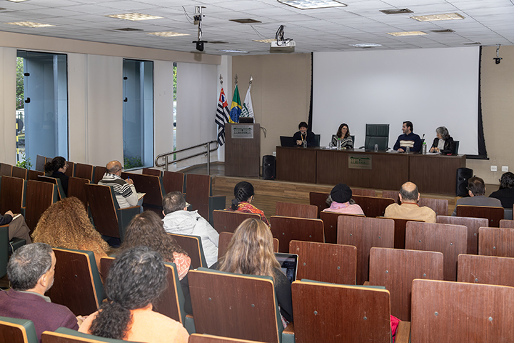 Público sentado assiste à mesa de debate no auditório, com painel de projeção ao fundo.