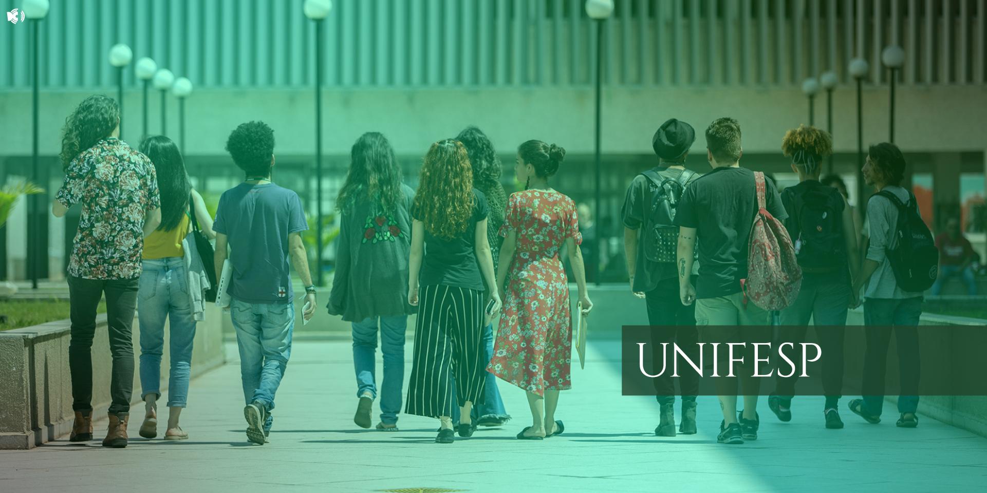 A imagem mostra um grupo de estudantes caminhando em direção a um prédio universitário durante o dia. Eles estão vestidos de maneira casual, carregando mochilas e alguns seguram cadernos ou notebooks. O ambiente tem postes de iluminação e uma arquitetura moderna ao fundo. Há uma sobreposição com tom esverdeado e a palavra "UNIFESP" destacada no canto direito, indicando que a imagem está relacionada à Universidade Federal de São Paulo.