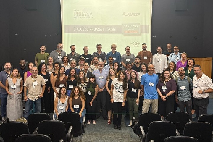 A imagem mostra um grupo grande de pessoas reunidas em um auditório para um evento. Ao fundo, há uma tela de projeção com a identificação do evento: "DIÁLOGOS PROASA I – 2025", que faz parte do programa "PROASA - Pesquisa em Saúde Planetária", associado à FAPESP (Fundação de Amparo à Pesquisa do Estado de São Paulo). A data na tela indica que o evento ocorreu em 20 de março de 2025, no Instituto de Matemática e Estatística da USP (IME-USP).  As pessoas na foto estão sorrindo e posando para a foto, sugerindo um clima descontraído e colaborativo. A maioria está usando crachás, indicando que são participantes do evento. A diversidade de idades e estilos sugere um encontro acadêmico ou científico com múltiplos representantes de diferentes áreas ou instituições.