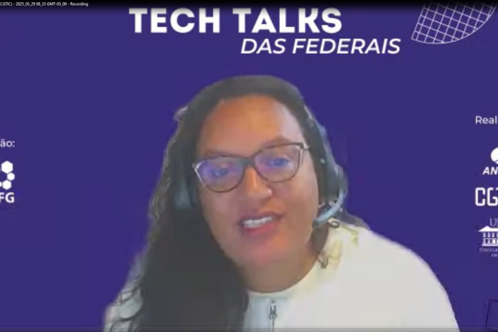 A imagem mostra uma mulher usando óculos e fones de ouvido com microfone, participando de uma videoconferência ou transmissão ao vivo. Ela está sorrindo e parece estar falando. O fundo é de cor roxa com textos e logotipos.  Na parte superior da imagem, lê-se em destaque: "TECH TALKS DAS FEDERAIS"