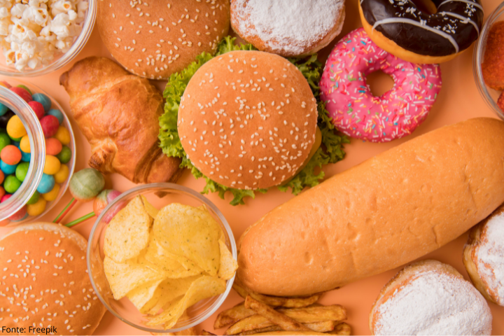 Imagem mostra diversos alimentos ultraprocessados, como hambúrguer, pipoca, batata frita e donuts